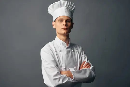 Профессиональный шеф-повар с серьезным выражением лица держит руки перед собой на темном фоне