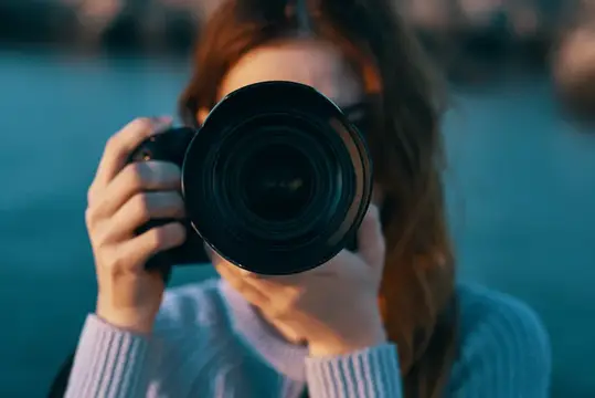Рыжеволосая девушка фотографирует через большой объектив камеры