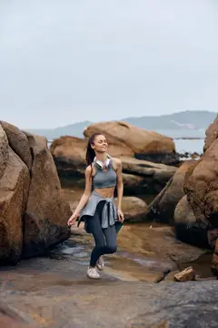 Спортивная девушка стоит на камнях у моря в пасмурный день