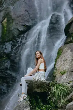 Улыбающаяся девушка сидит на камне у водопада