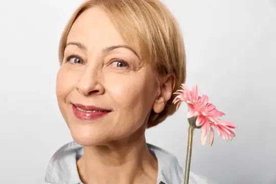 Улыбающаяся блондинка зрелого возраста с розовой герберой у лица