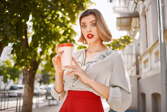 Блондинка в красной юбке на открытом воздухе с чашкой кофе веселится