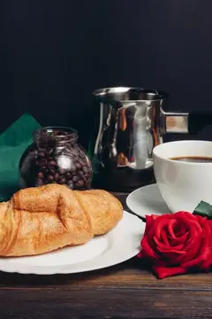 Круассан, чашка кофе и алая роза на тёмном столе