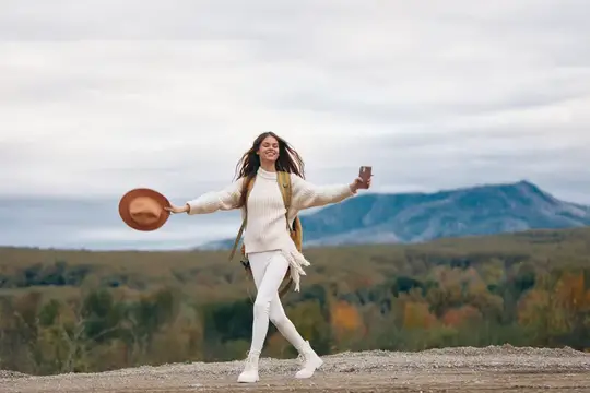 Улыбающаяся девушка с шляпой и стаканом гуляет на фоне гор
