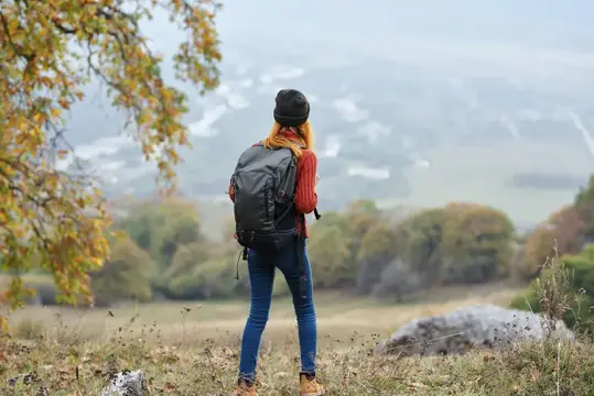 Девушка с рюкзаком смотрит на осенние горы