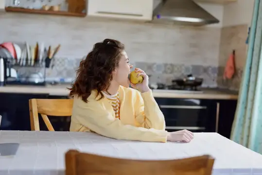 Кудрявая девушка в жёлтом свитере пьёт сок на кухне