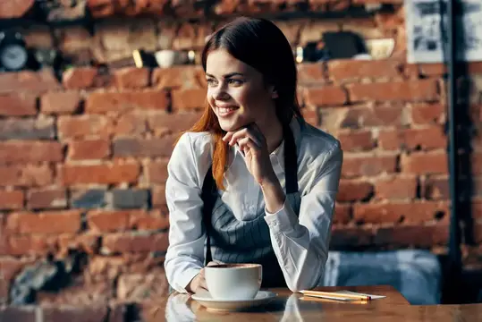 Улыбающаяся девушка в фартуке за столиком кофейни