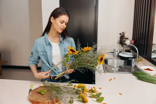 Молодая женщина составляет букет из подсолнухов на кухне