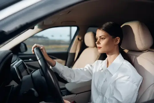 Молодая женщина в белой рубашке за рулём автомобиля