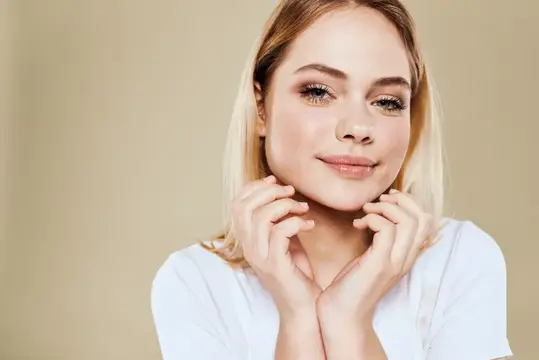 Светловолосая девушка с макияжем нежно улыбается на бежевом фоне