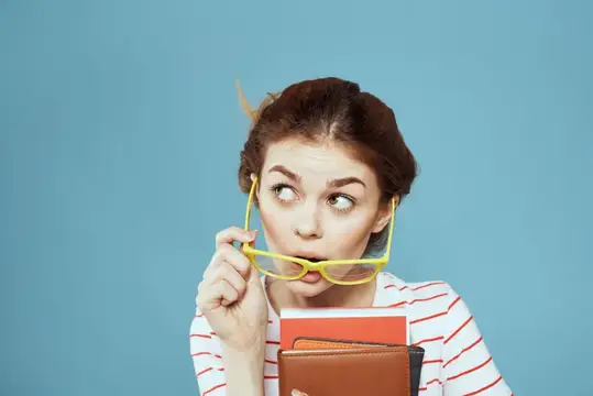 Рыжеволосая девушка с книгами удивлённо выглядывает из-за жёлтых очков