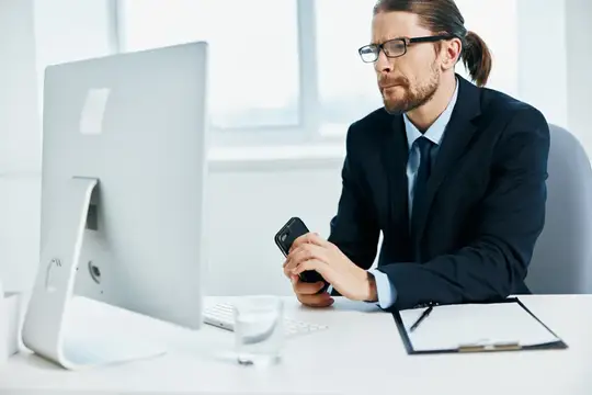 Мужчина в очках и деловом костюме работает за компьютером в офисе