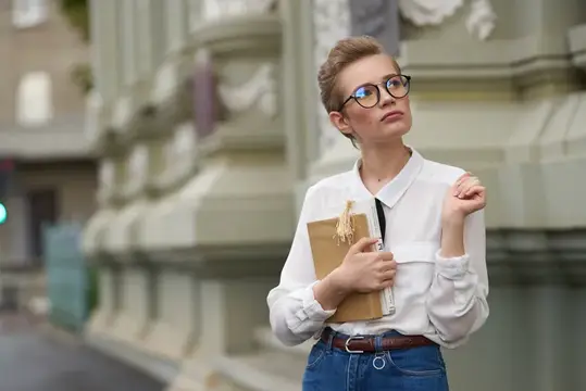 Молодая женщина в очках с блокнотом на фоне старинного здания