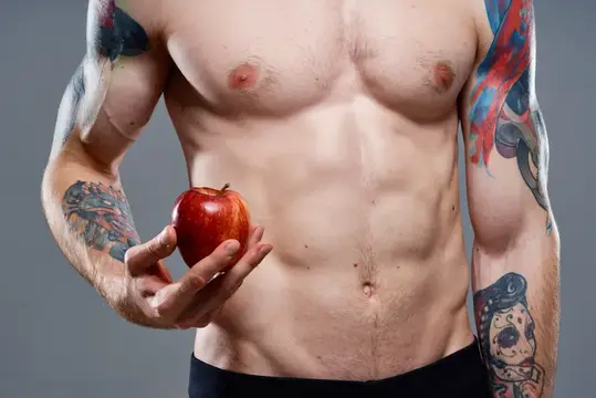 Мускулистый мужчина с татуировками держит красное яблоко