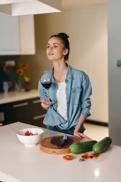 Молодая женщина с бокалом красного вина на кухне