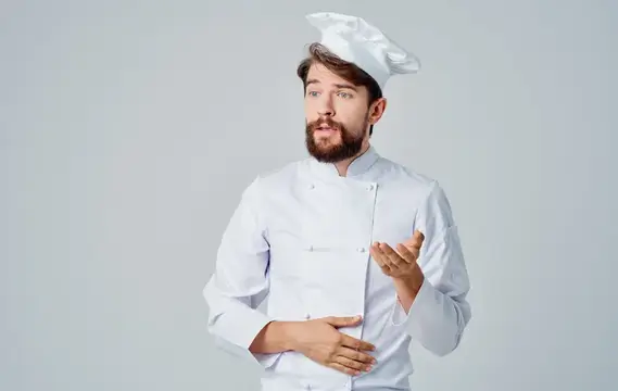 Бородатый повар в белом колпаке жестикулирует на сером фоне