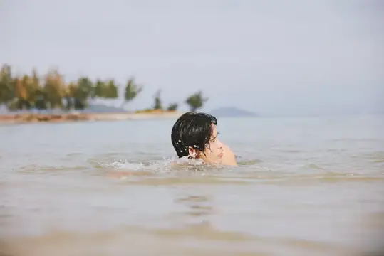Молодой человек с мокрыми тёмными волосами купается в море