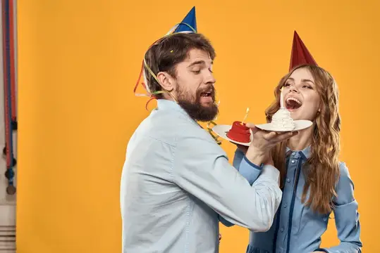 Мужчина и женщина на вечеринке в колпаках с тортом и мишурой на жёлтом фоне
