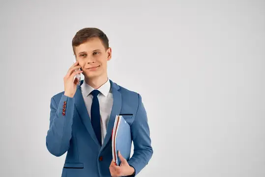 Молодой человек в синем костюме говорит по телефону с папкой