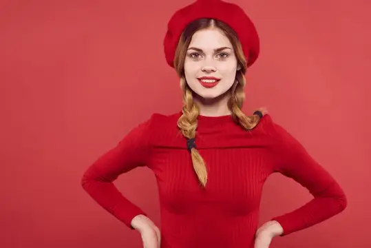 Молодая женщина в красном берете и платье с косами на красном фоне
