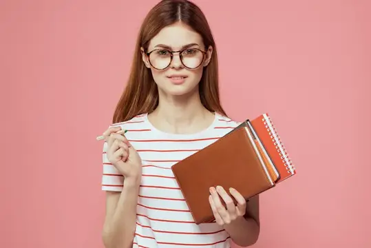 Девушка-студентка с блокнотами на розовом фоне жестикулирует руками
