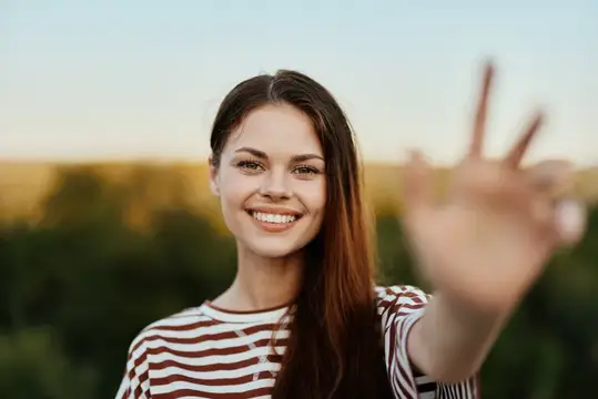 Улыбающаяся темноволосая девушка машет рукой на закате