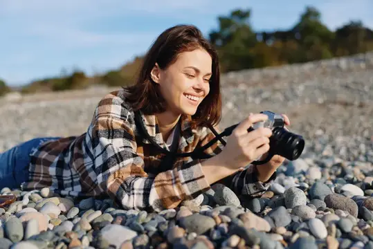Улыбающаяся девушка лежит на каменистом пляже с фотокамерой