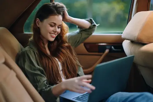 Улыбающаяся девушка с ноутбуком на заднем сиденье автомобиля