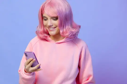 Улыбающаяся девушка с розовыми волосами смотрит в смартфон на сиреневом фоне