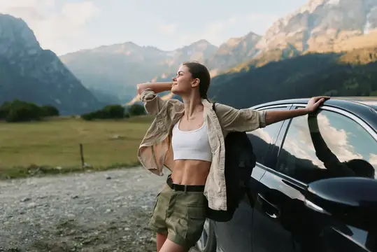 Молодая женщина отдыхает у автомобиля на фоне гор