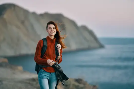 Улыбающаяся девушка с рюкзаком гуляет по берегу моря