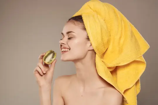 Улыбающаяся девушка с жёлтым полотенцем на голове нюхает половинку лайма