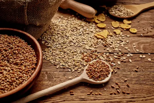 Деревянная ложка с зерном на фоне рассыпанных хлопьев и крупы