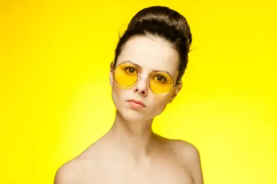 Симпатичная женщина в забавных жёлтых очках с обнажёнными плечами на изолированном фоне