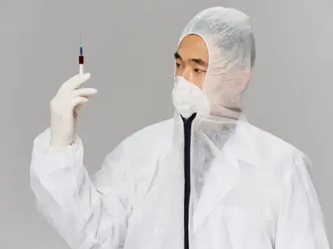 Мужчина в защитном костюме держит шприц с вакциной