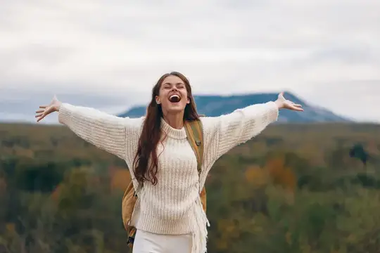 Счастливая девушка с рюкзаком раскинула руки на фоне гор
