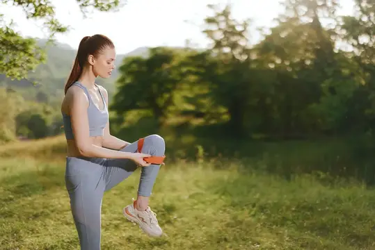 Спортивная девушка с резинкой тренирует ноги на лугу
