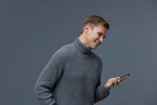 Улыбающийся мужчина в сером свитере смотрит в смартфон