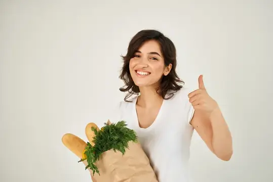 Улыбающаяся брюнетка с пакетом продуктов показывает большой палец вверх
