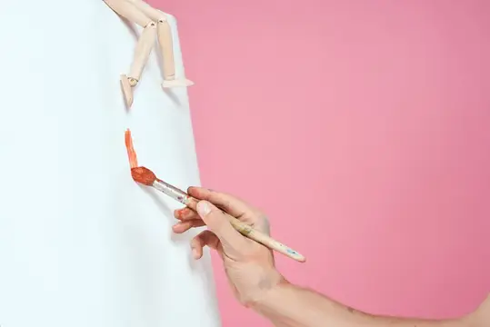 Рука с кистью рисует оранжевой краской на белом фоне
