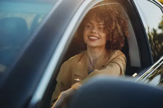 Улыбающаяся кудрявая девушка выглядывает из окна автомобиля