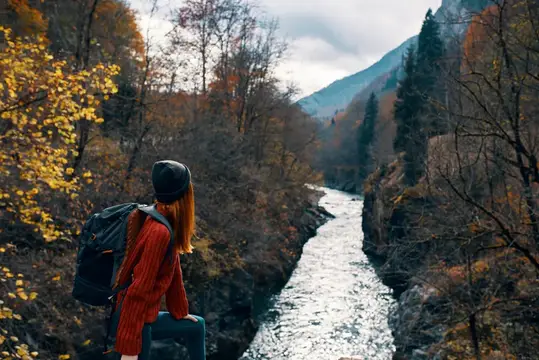 Женщина-туристка с рюкзаком стоит в горах в осеннем лесу