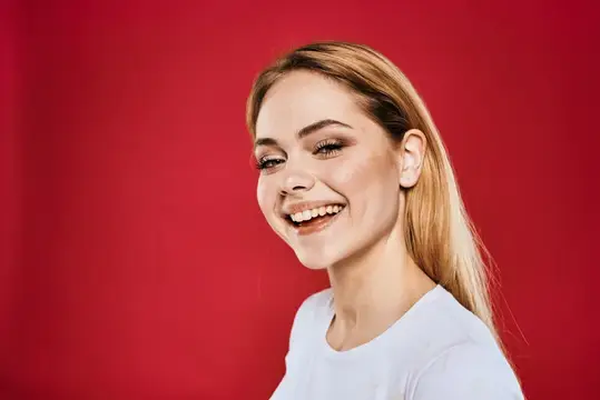 Светловолосая девушка искренне улыбается на красном фоне