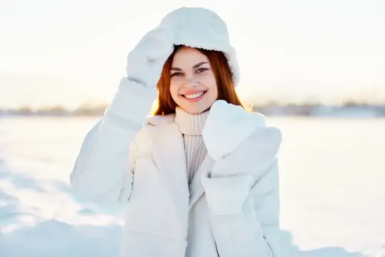 Улыбающаяся девушка в белой шапке и пуховике на зимнем снегу