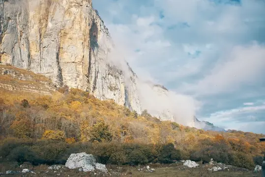 Осенние деревья у подножия скалы в облаках