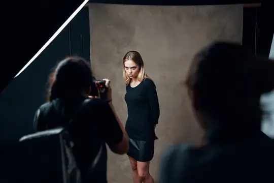 Фотограф снимает модель в чёрном платье в студии