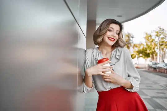 Улыбающаяся женщина с кофе в руках стоит у стены здания