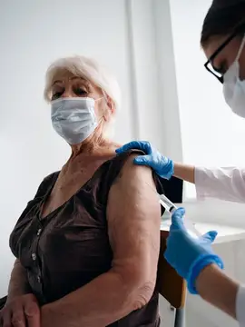 Врач делает инъекцию вакцины от COVID-19 женщине-пациентке, которая держит паспорт вакцинации