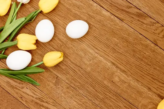 Желтые тюльпаны и белые яйца на деревянном столе