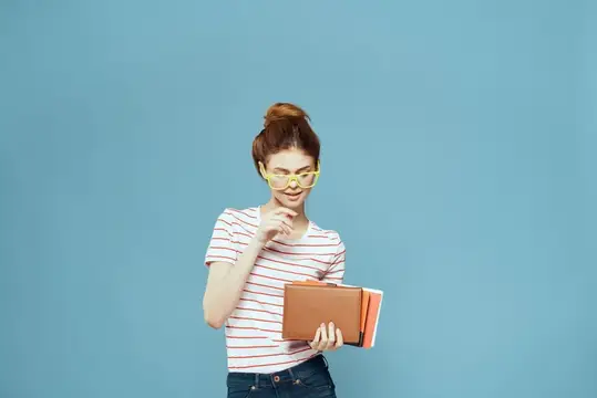Рыжеволосая девушка в жёлтых очках с книгой на голубом фоне
